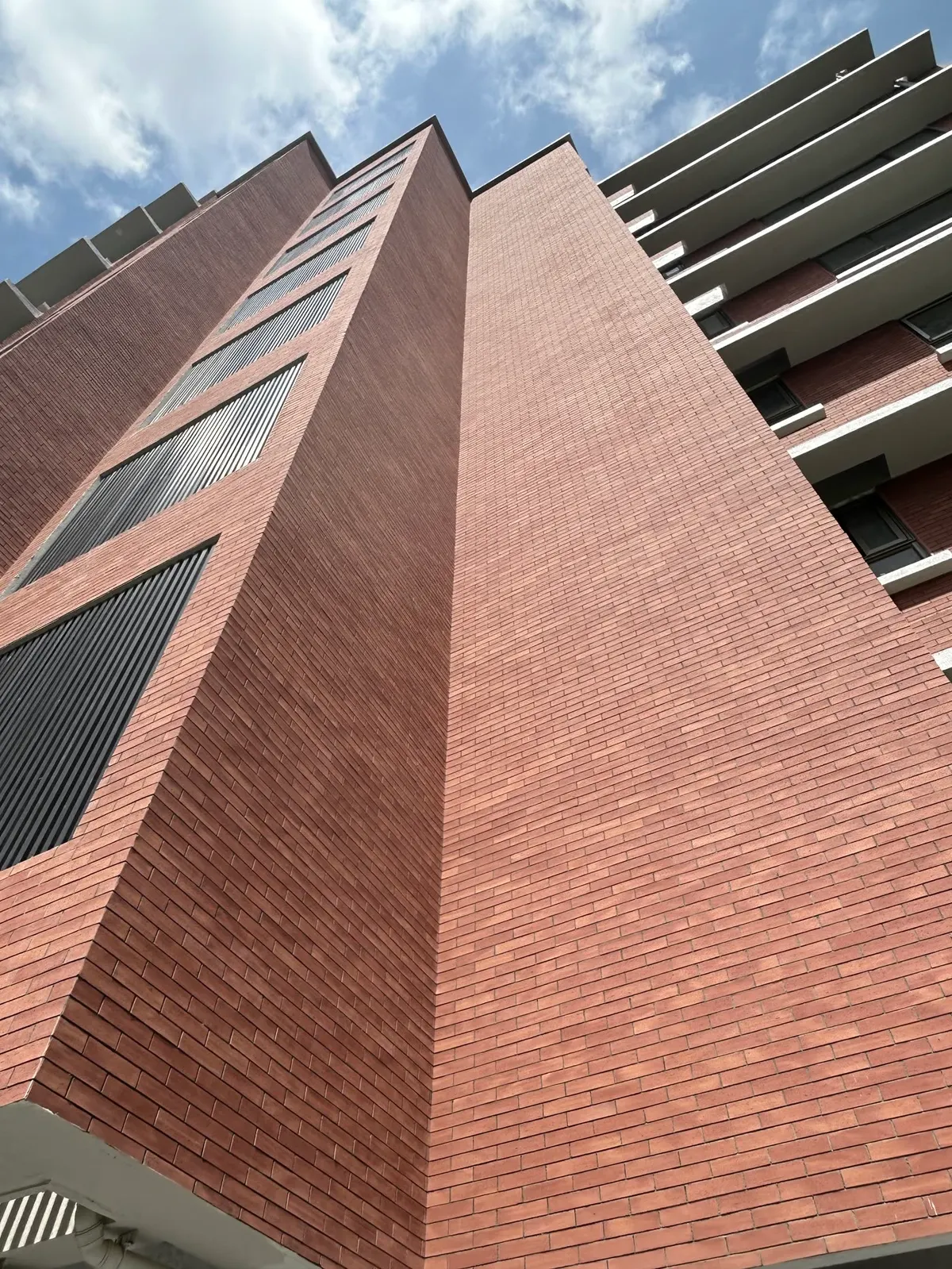 Esquina de edificio alto con piel de ladrillo delgado y balcones blancos